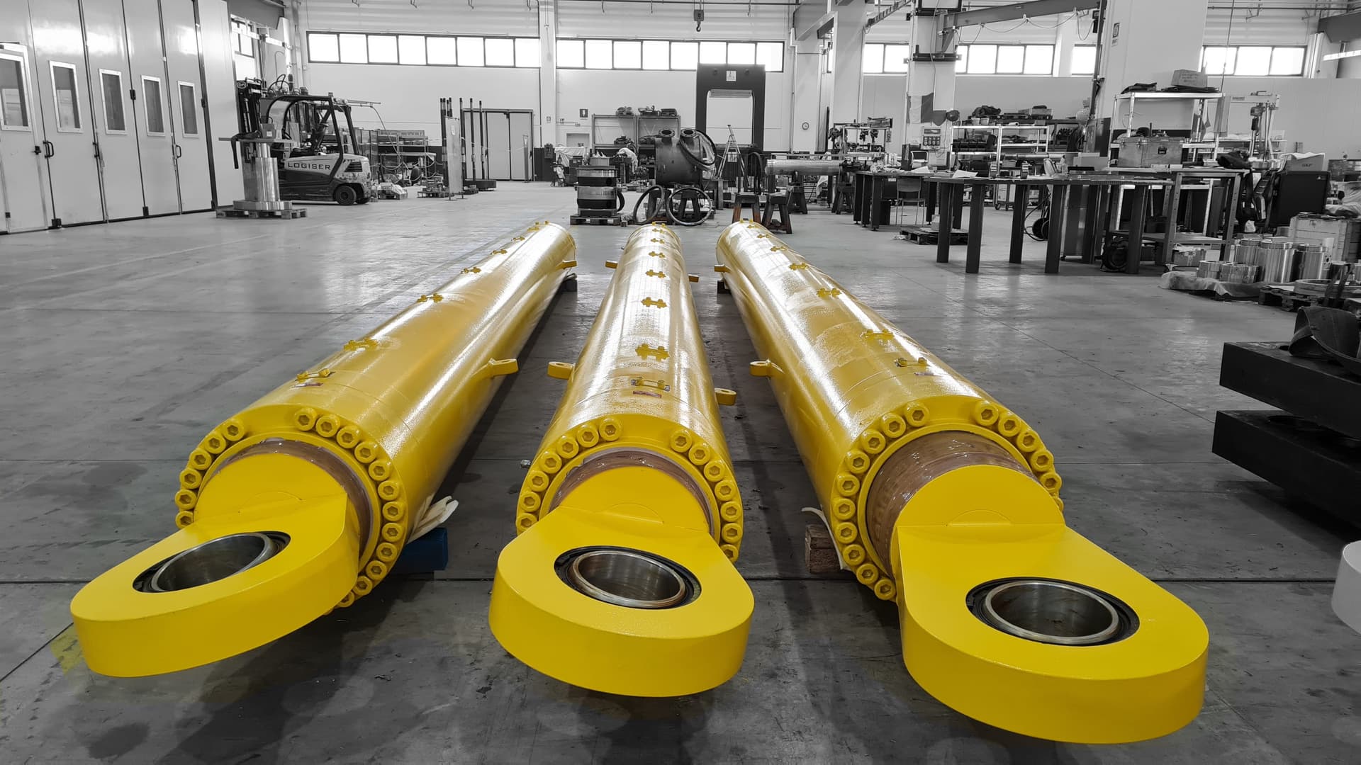 Three yellow hydraulic cylinders lying in a workshop