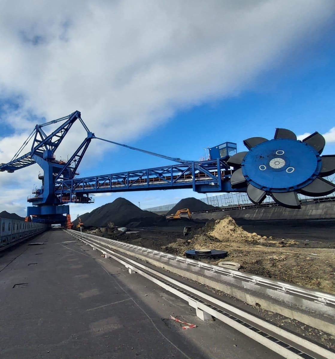 Stacker-reclaimer bleu avec flèche et roue à godets dans une installation de manutention