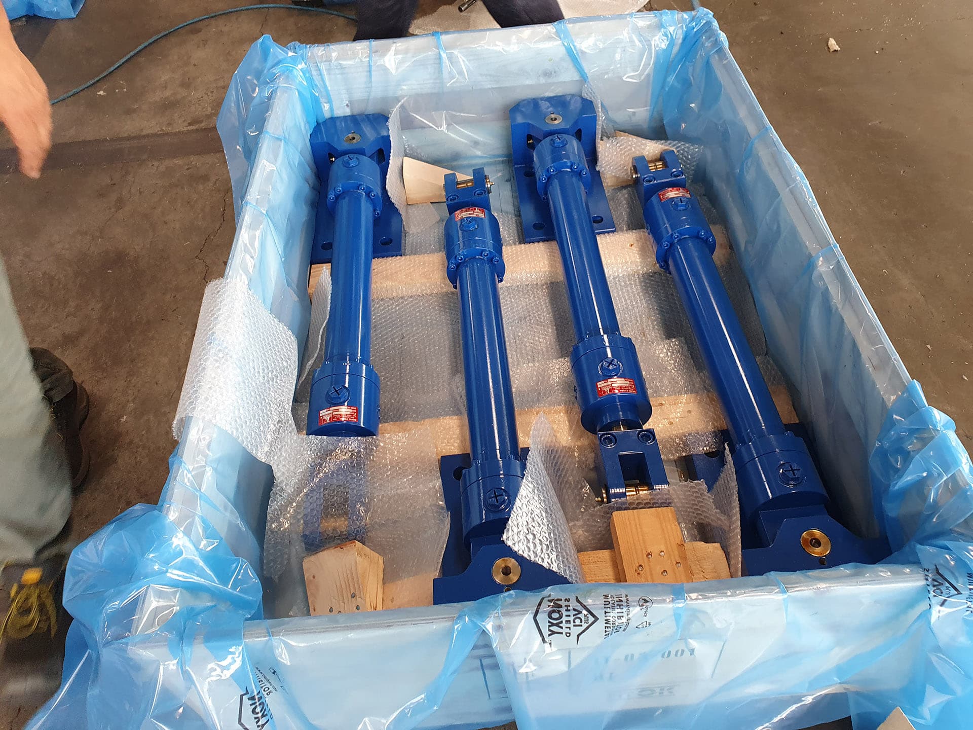 Four blue cylinders wrapped in protective film inside a wooden packing case