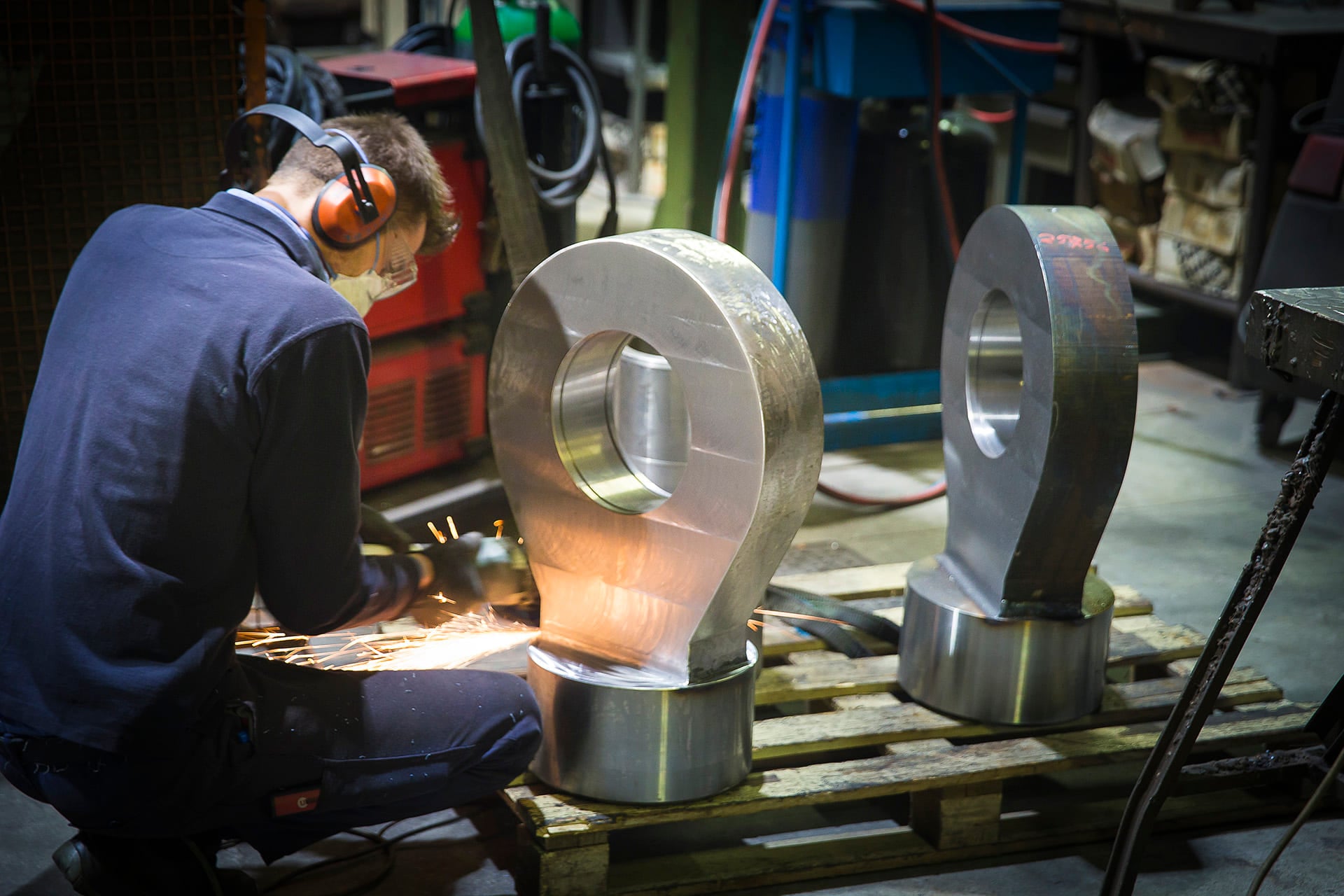 Operator working on two large forged rod-end eyes in a workshop
