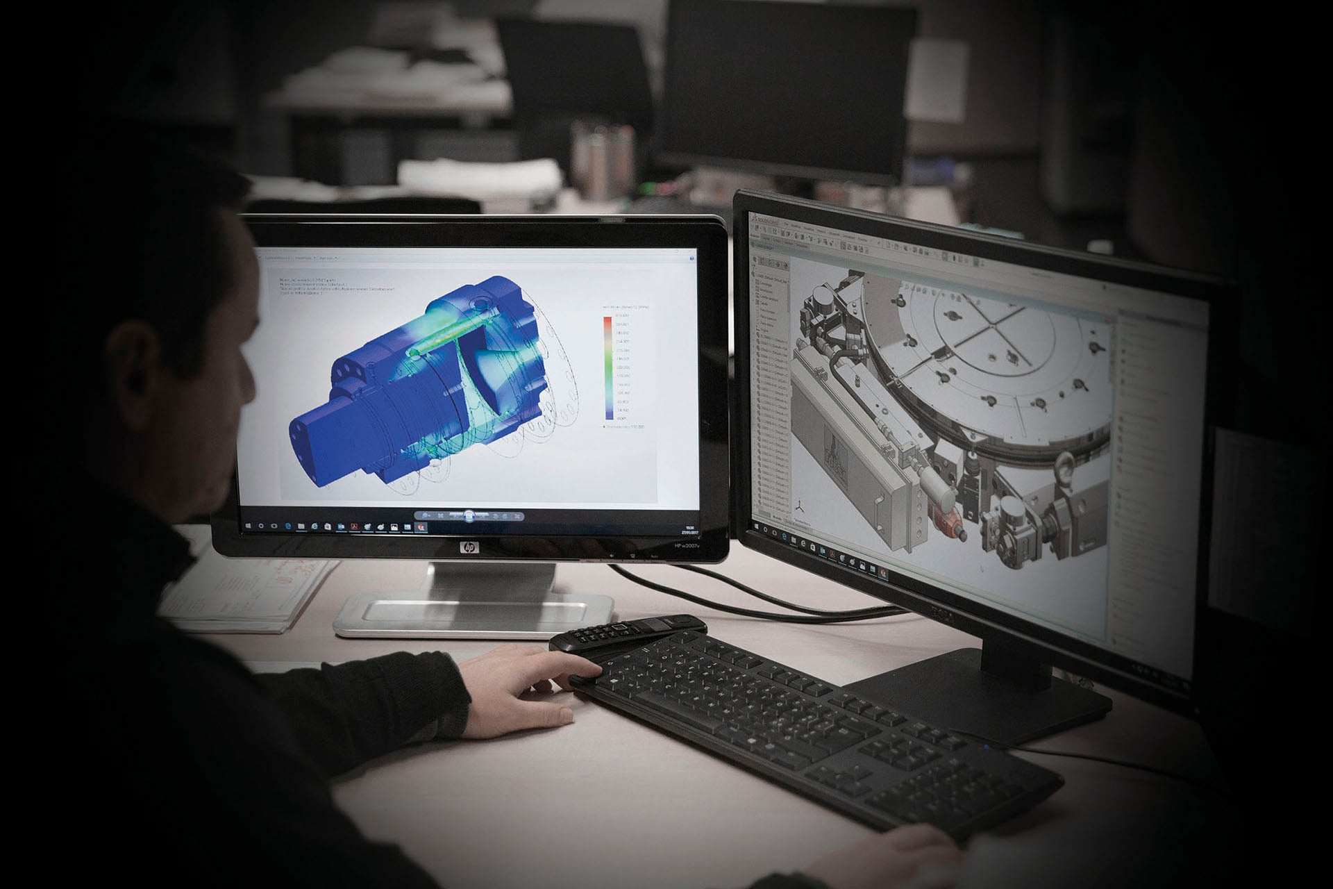 Engineer working with CAD and stress analysis software on two monitors
