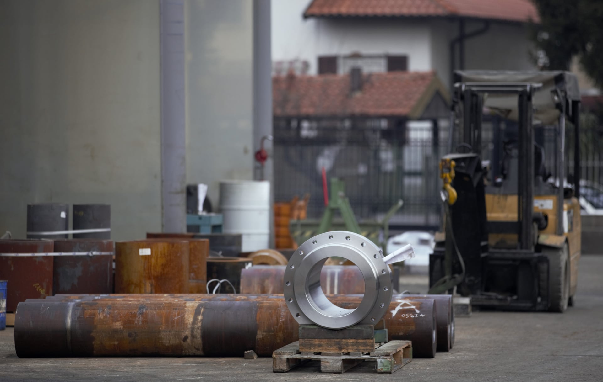 Anello in acciaio lavorato su un supporto in un piazzale con grandi tubi e un carrello elevatore