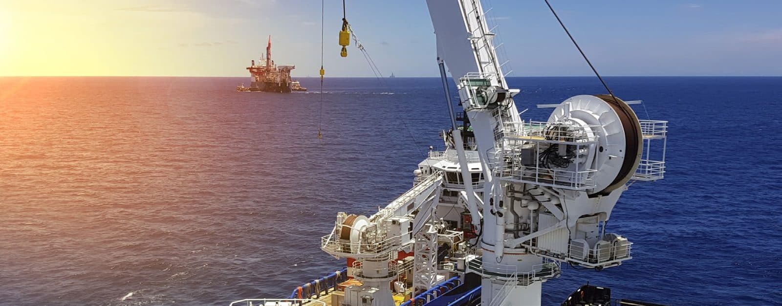Offshore crane on a vessel at sunset, with a platform on the horizon