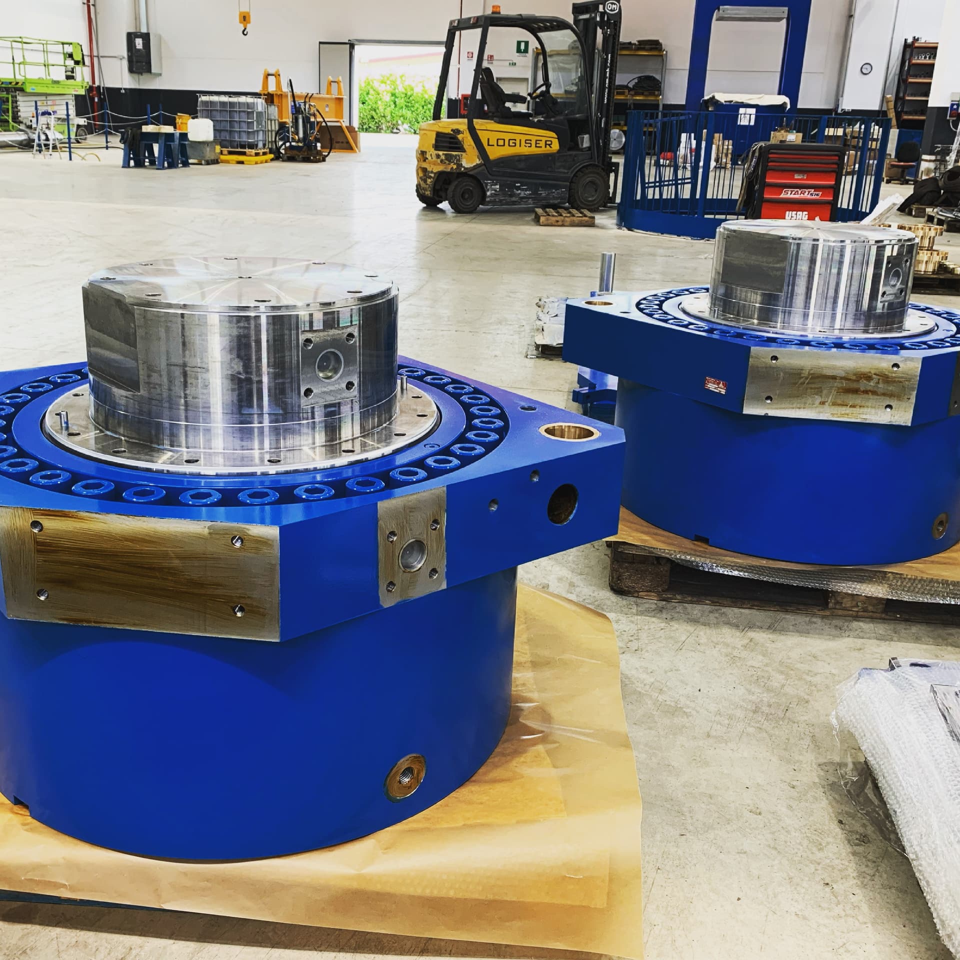 Two blue hydraulic capsules with machined steel pistons in a workshop