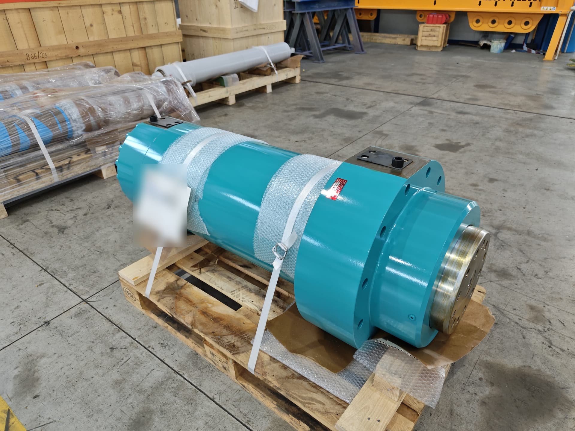 Light blue hydraulic cylinder protected with bubble wrap and strapped to a pallet for shipping