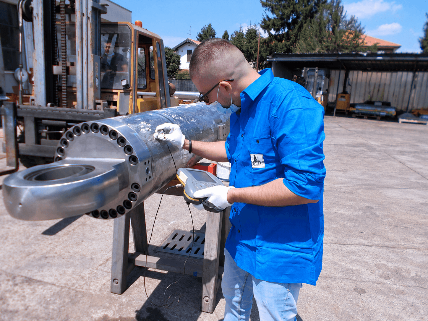 Technician in a blue shirt checking a large cylinder with a handheld instrument