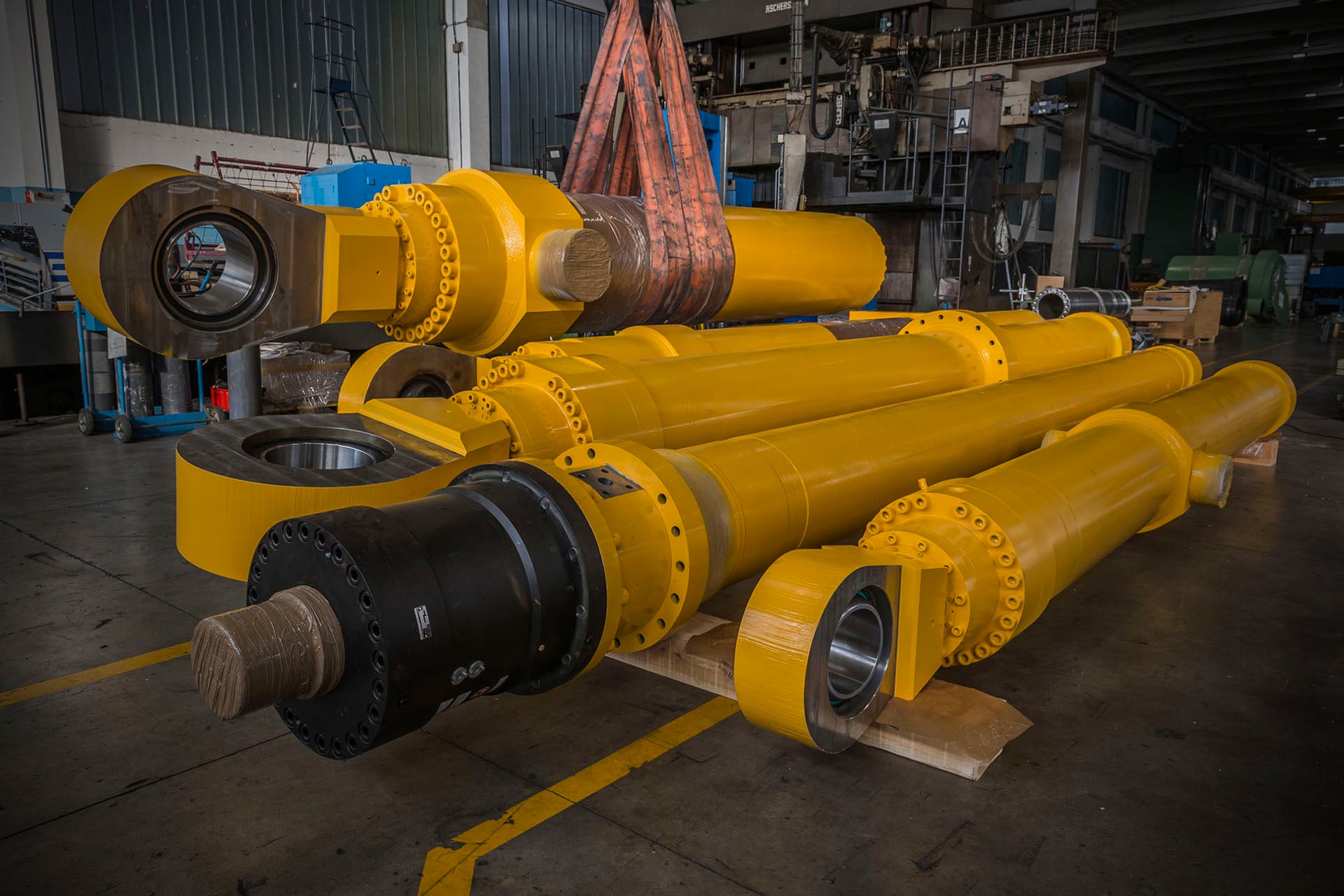 Large yellow hydraulic cylinders with rod eyes lying in a workshop
