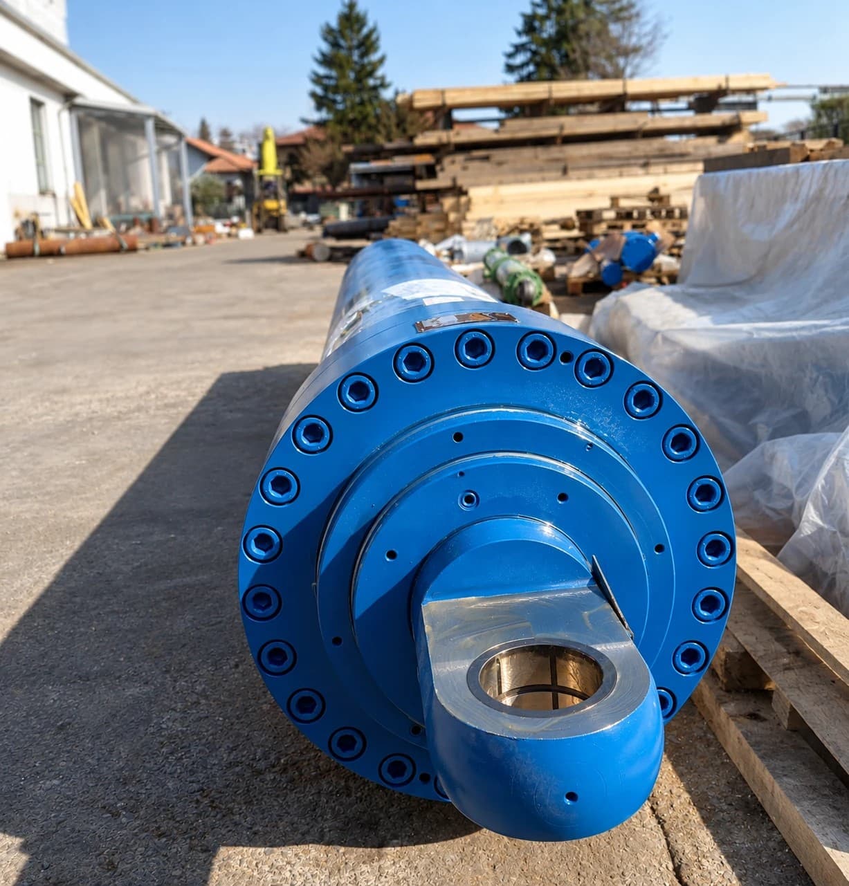 Blue large-diameter cylinder end with a bolted flange and rod-end eye, outdoors