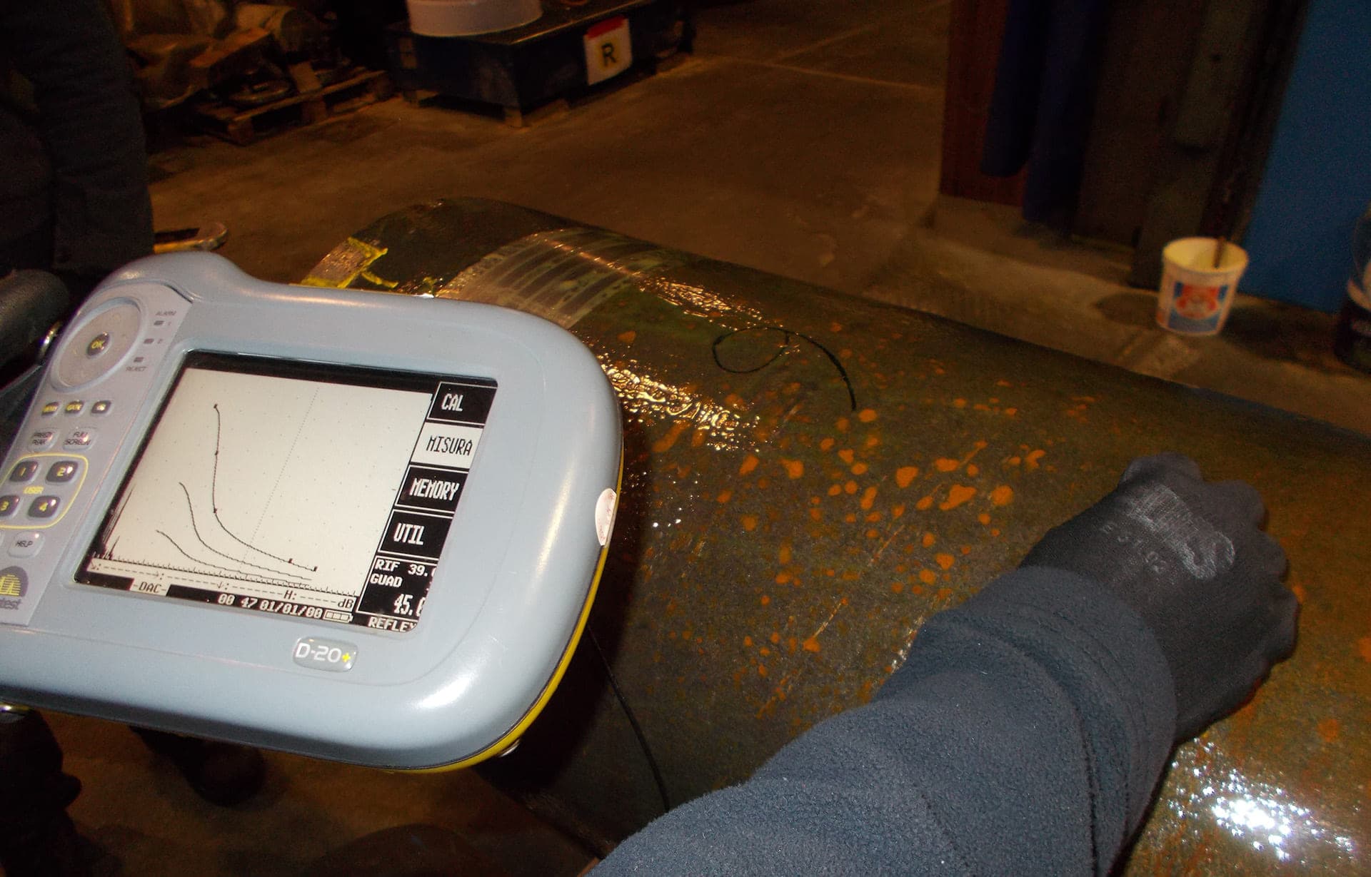 Technician holding a portable measuring instrument against a large cylinder