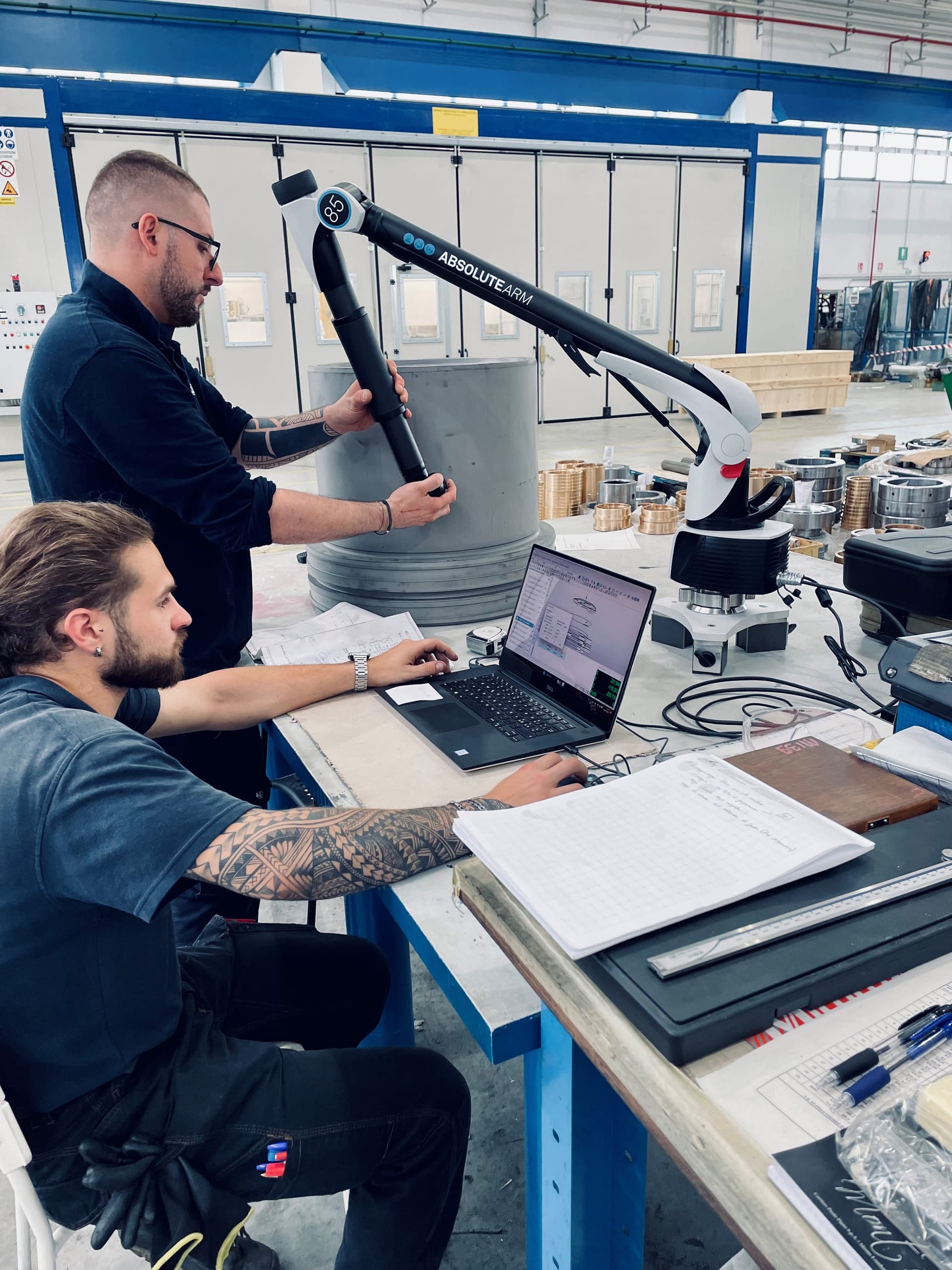 Two technicians using a portable measuring arm and a laptop for dimensional checks