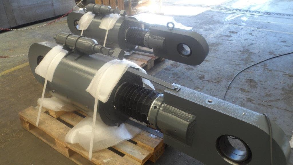 Two grey hydraulic seismic devices with clevis eyes and bellows, ready for shipment