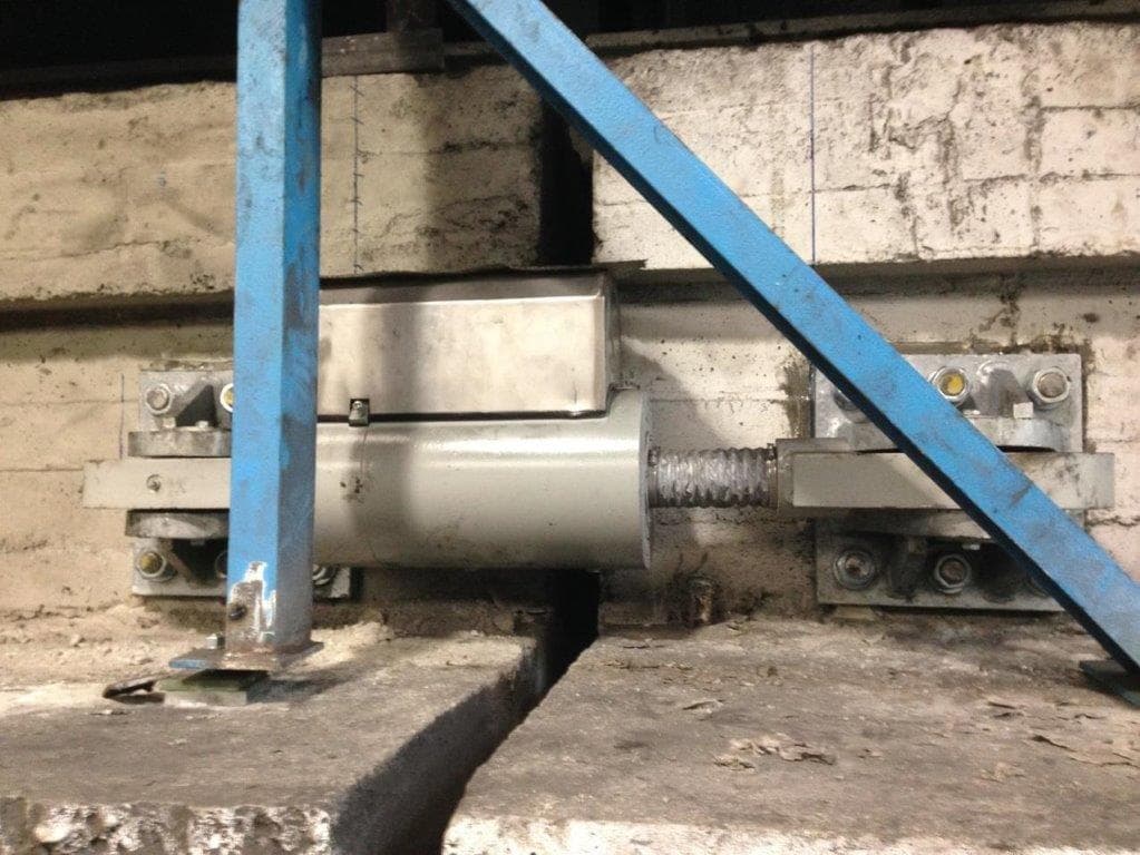 Hydraulic seismic device mounted across a joint in a concrete structure