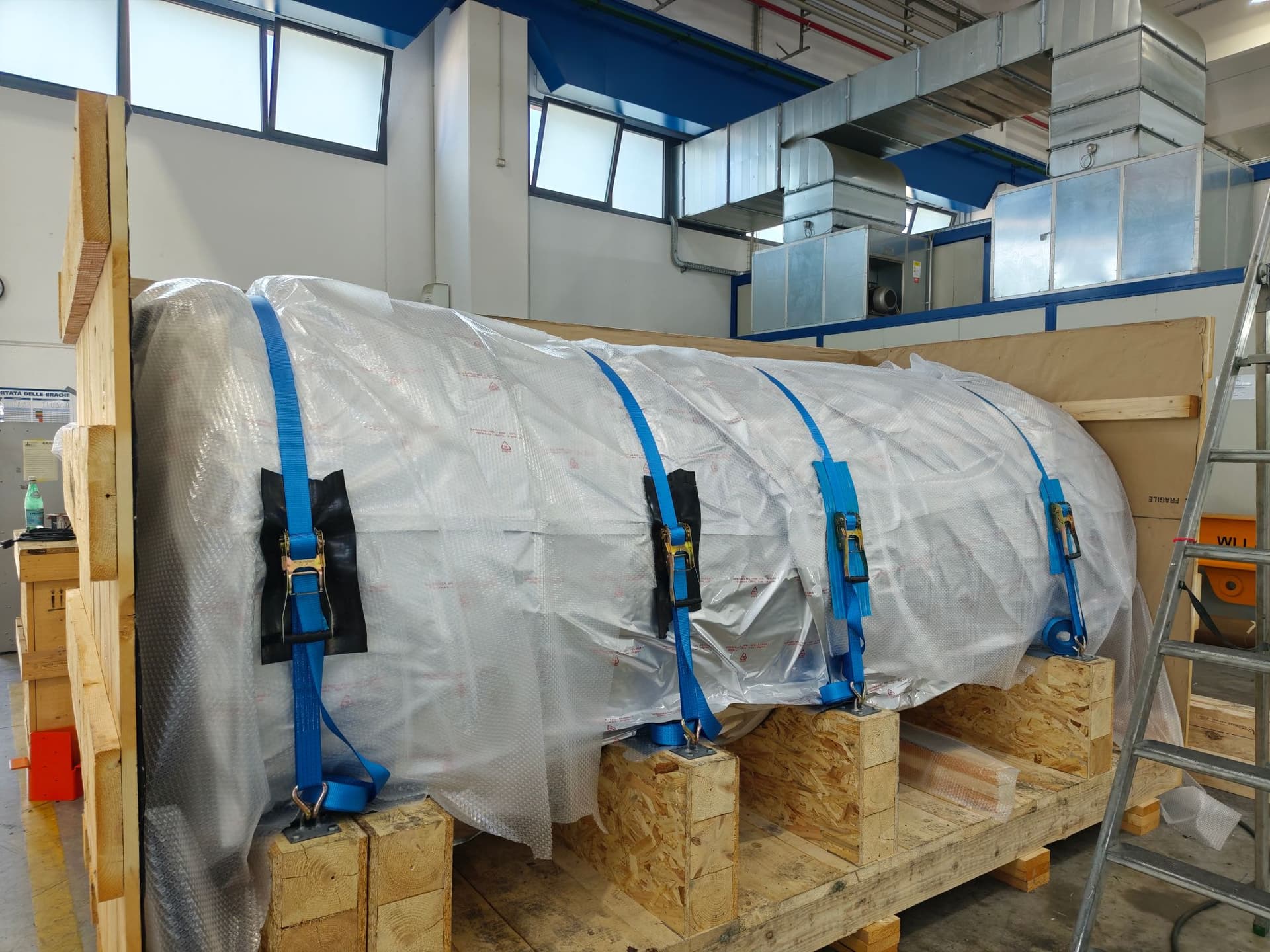 Large cylinder wrapped in protective film and strapped onto wooden supports inside a shipping crate