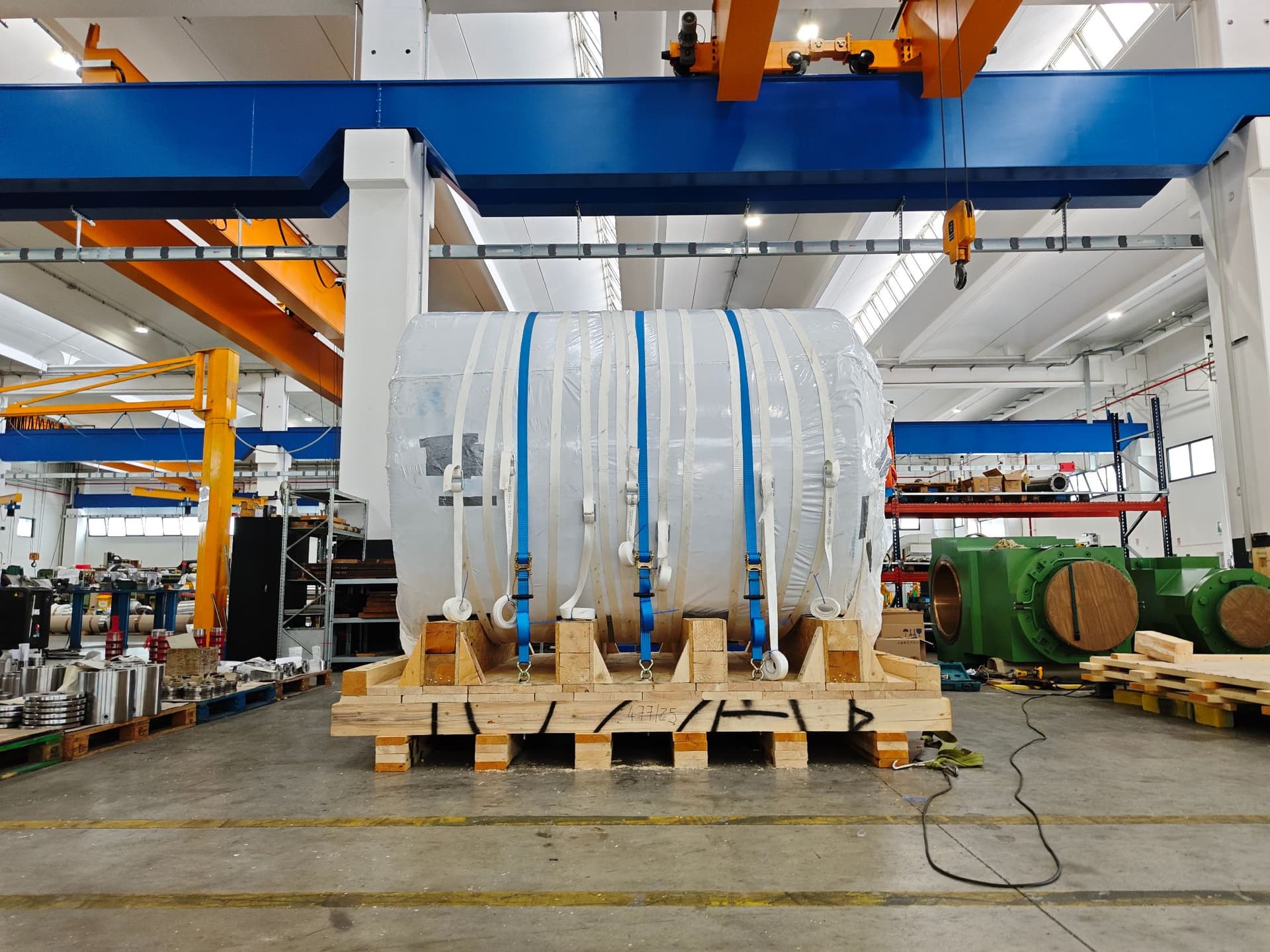 Large cylinder wrapped in white film and secured with straps on a wooden shipping skid, front view