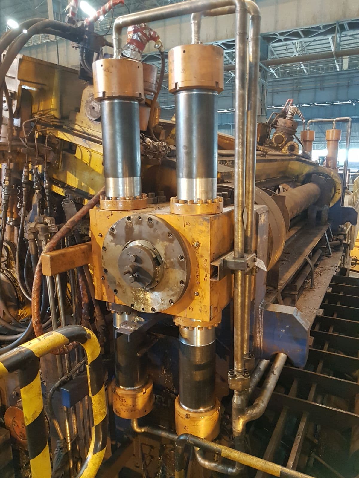 Two chrome cylinder rods entering a yellow-orange cylinder head in an industrial plant