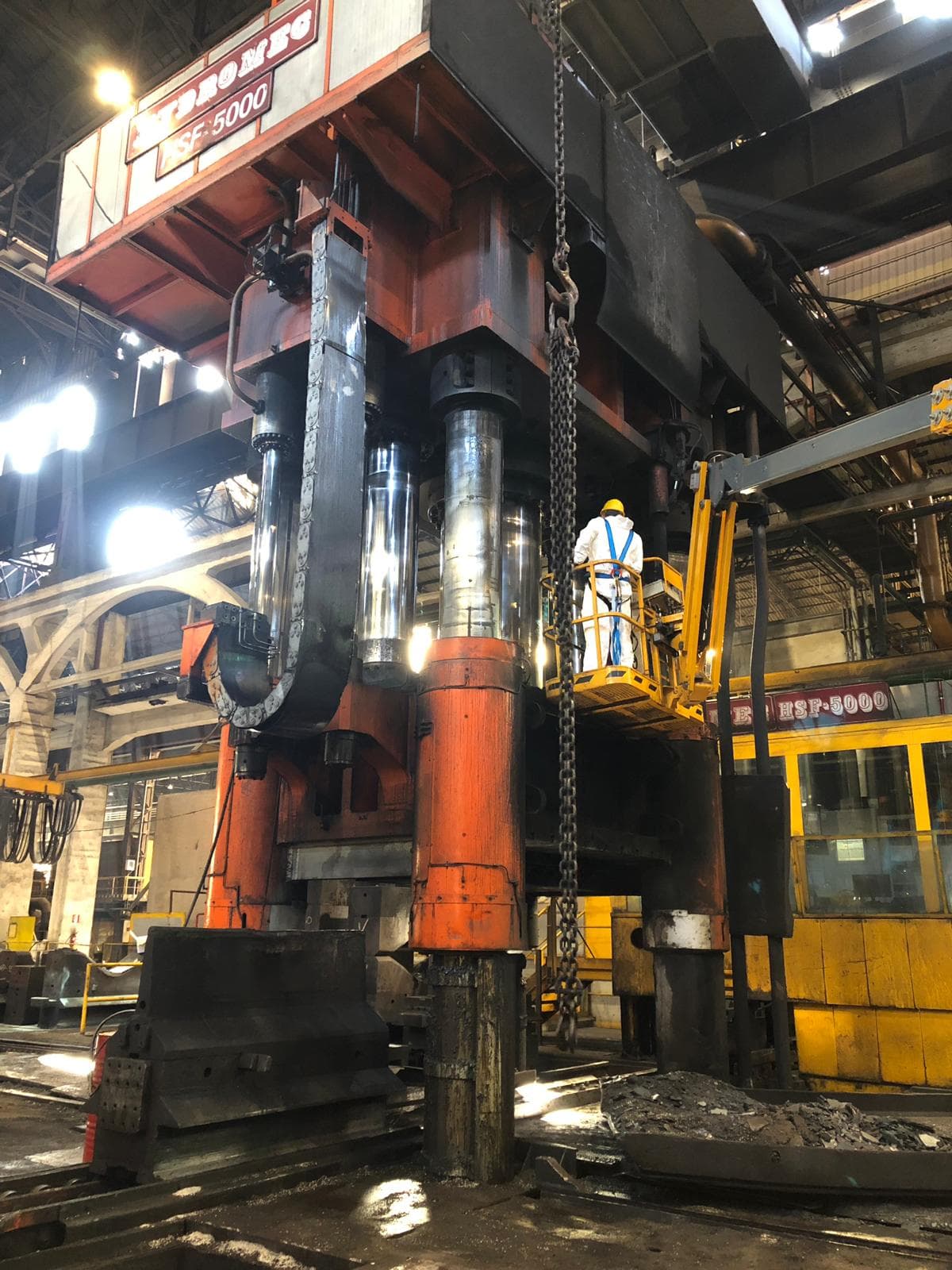 Technician on a lifting platform next to large red hydraulic press cylinders