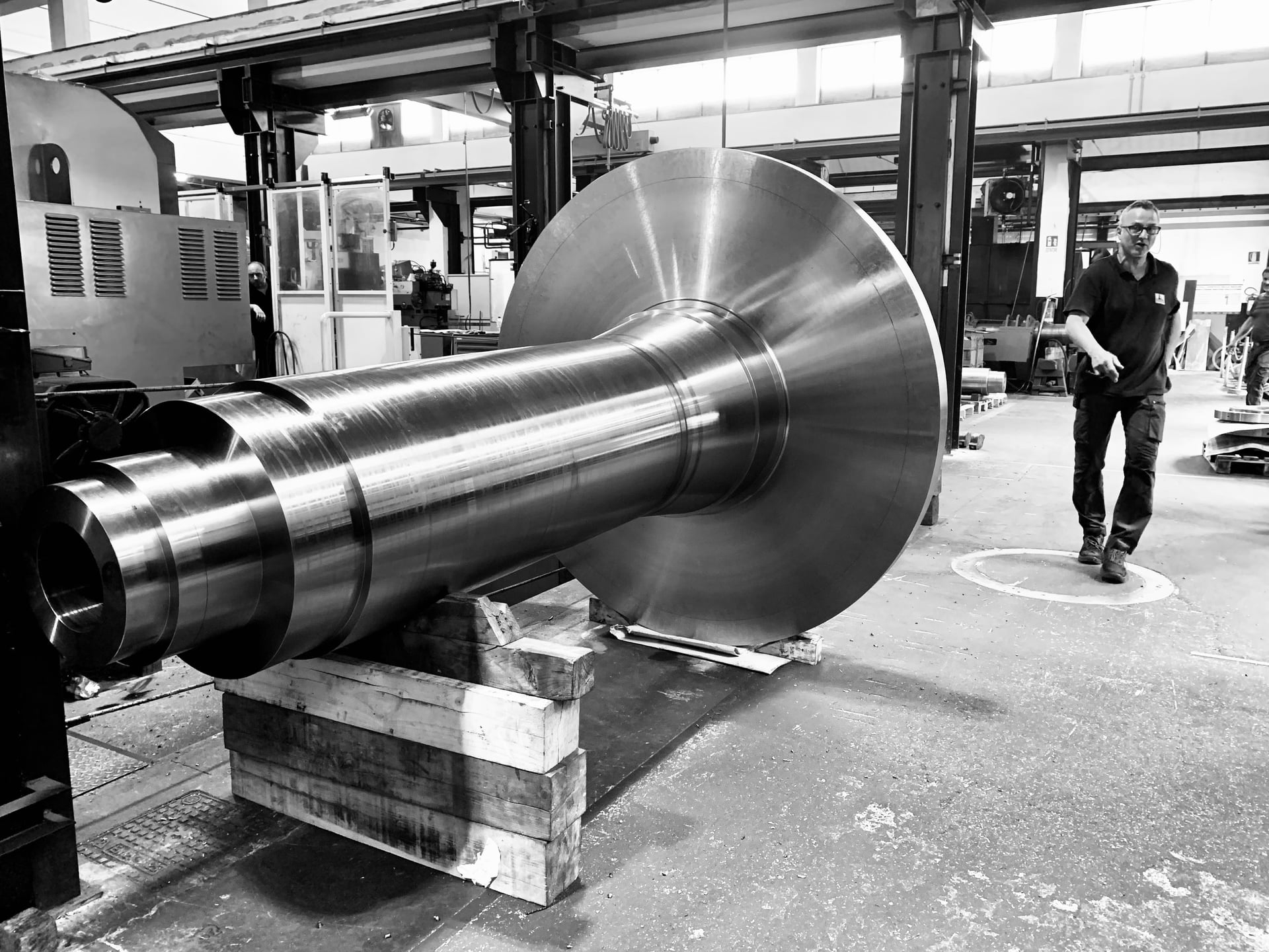 Photo en noir et blanc d'un grand arbre en acier forgé avec un disque sur un support